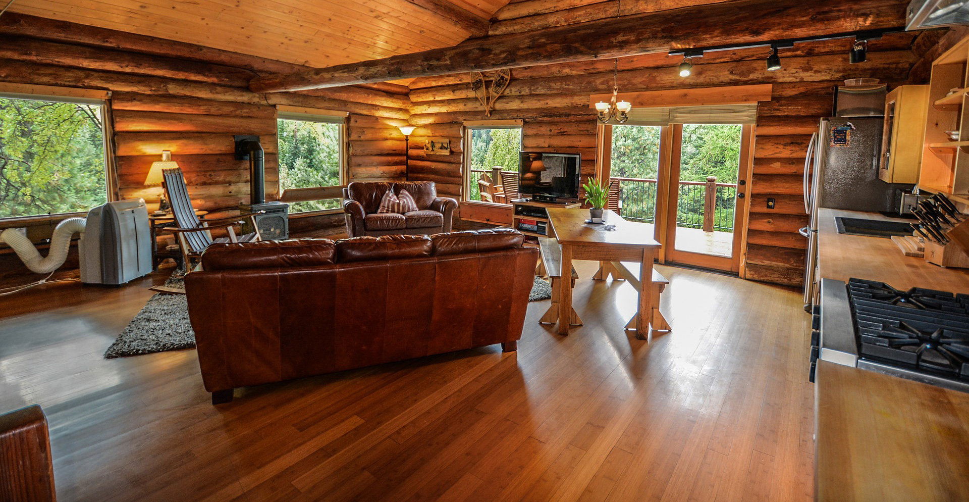 Intérieur chaleureux d’un chalet en bois, avec salon, cuisine et grandes fenêtres sur la forêt